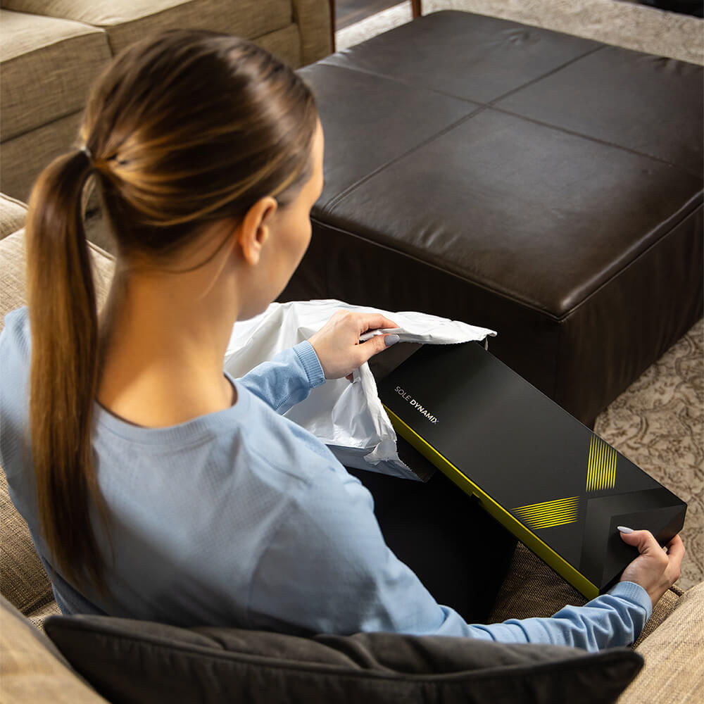 A woman receiving her order of Sole Dynamix custom insoles at home.