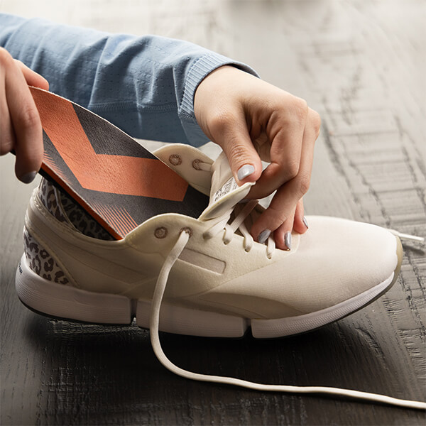 A woman sliding her new Sole Dynamix custom insole into her sneaker after trimming it to fit.